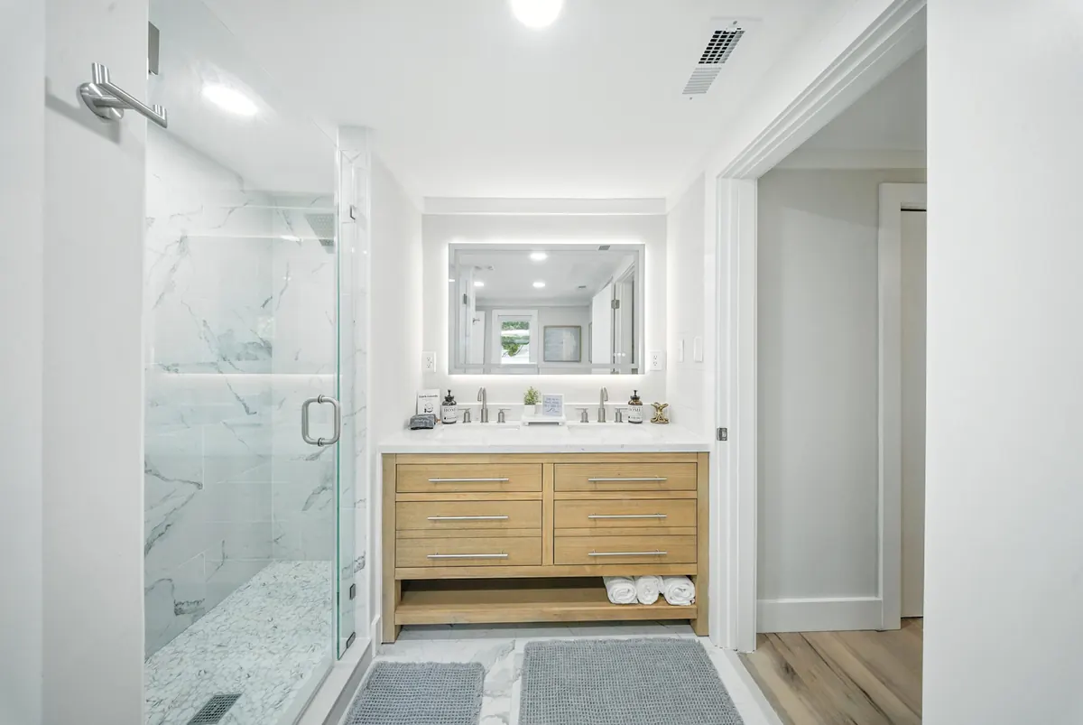 Modern bathroom with a wood vanity, backlit mirror and glass shower, photographed by Luma Real Estate Media