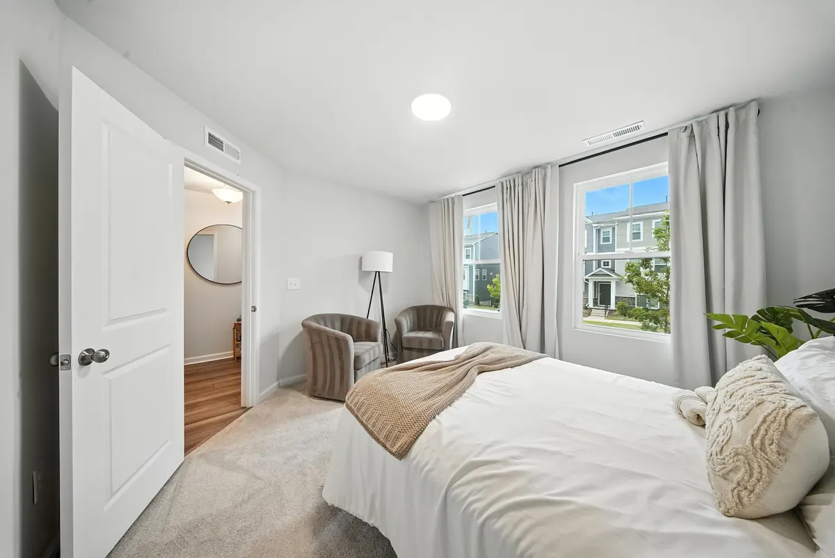 Charlotte guest bedroom with neutral bedding, accent chairs and two windows, photographed by Luma Real Estate Media